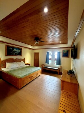 A bedroom with a wooden ceiling, a bed with a green bedspread, a bench, a wooden dresser, and a ceiling fan. - Inntayon Lodge Baguio City (Baguio)