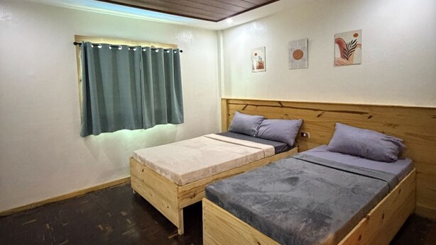 A room with two wooden beds, a small bench, a window with curtains, and three wall-mounted artworks. - Inntayon Lodge Baguio City (Baguio)