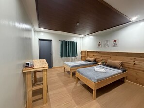 Una habitación con dos camas, una mesa de madera, una puerta y un techo con vigas de madera.