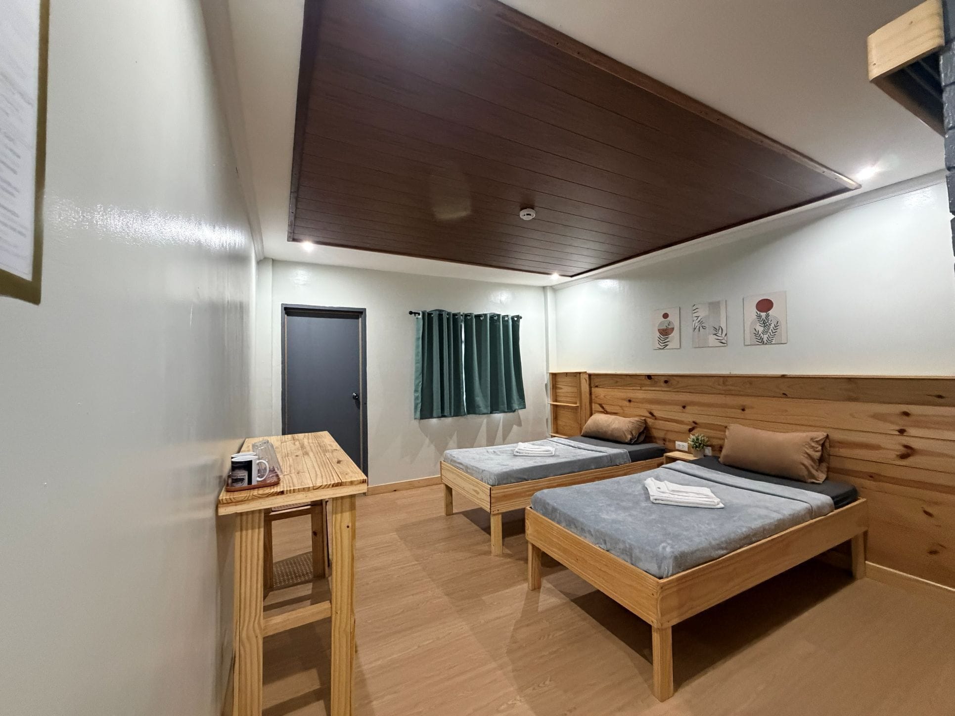 A room with two single beds, a wooden headboard, a small table with a cup and a glass, and a door with a curtain.