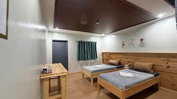 A room with two single beds, a wooden headboard, a small table with a cup and a glass, and a door with a curtain.