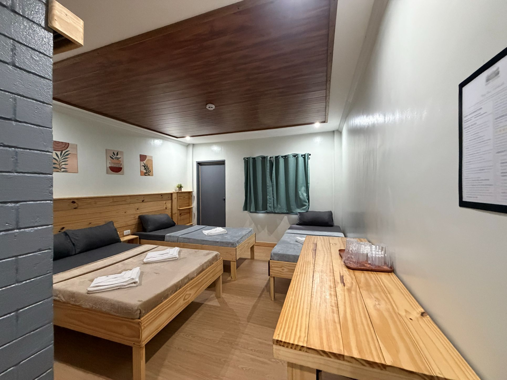 Una habitación con dos camas, una mesa de madera, una cortina verde y una pizarra en la pared.