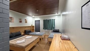 Una habitación con dos camas, una mesa de madera, una cortina verde y una pizarra en la pared.