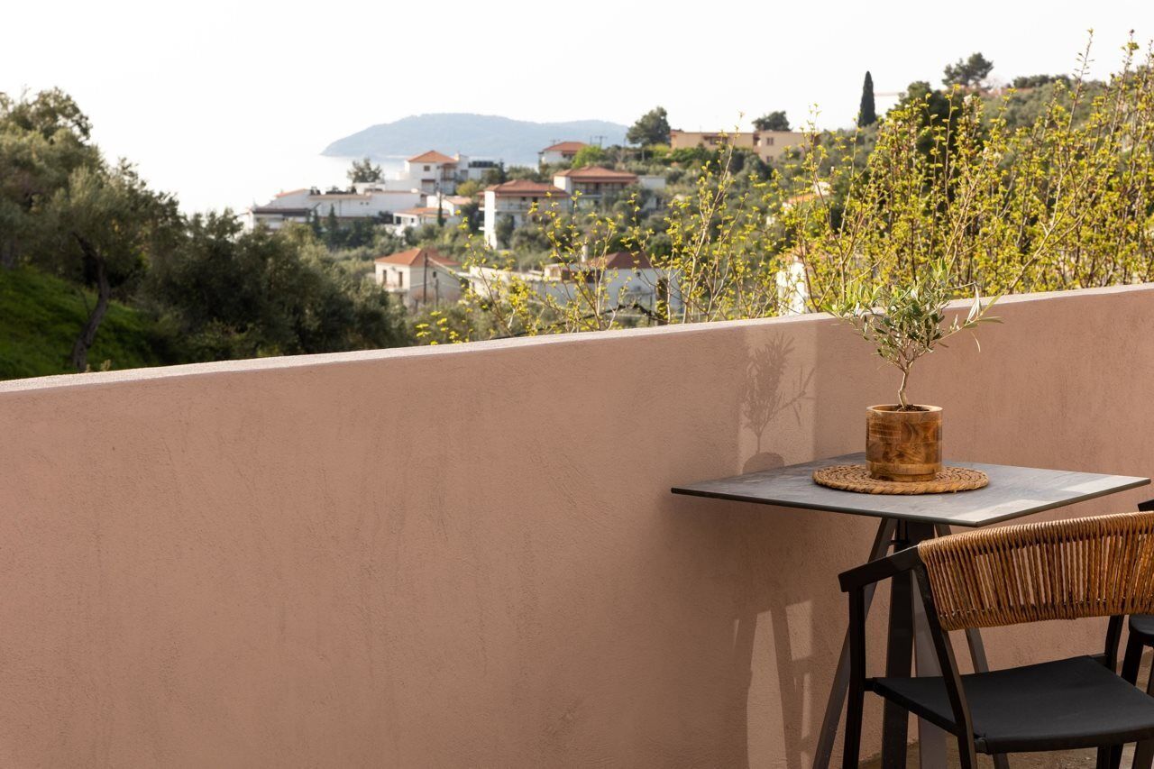 Un balcone con tavolo e sedia, una pianta in vaso e vista su un pendio con edifici.