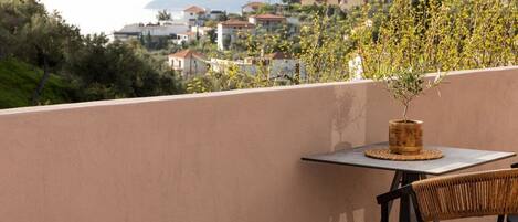 Un balcone con tavolo e sedia, una pianta in vaso e vista su un pendio con edifici.