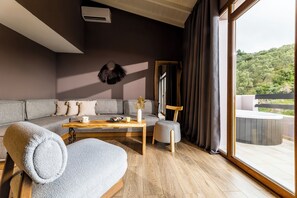 Una sala de estar moderna con un sofá, una mesa de centro y una silla. Hay un ventanal con cortinas y vistas a un balcón.