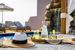 En avslappnad miljö vid poolen med solstolar, ett brickbord med glas och en dekorativ vattenfallsanordning.
