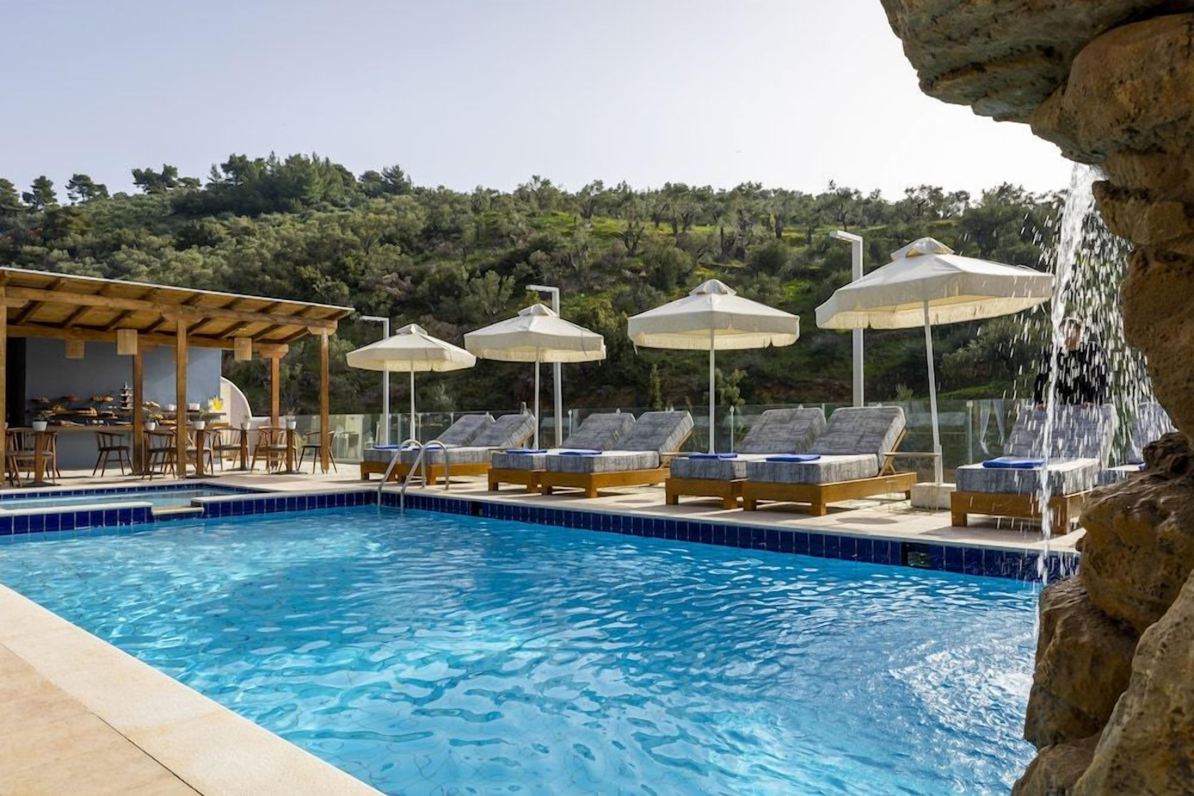Piscina com espreguiçadeiras e guarda-sóis, emoldurada por uma paisagem natural.