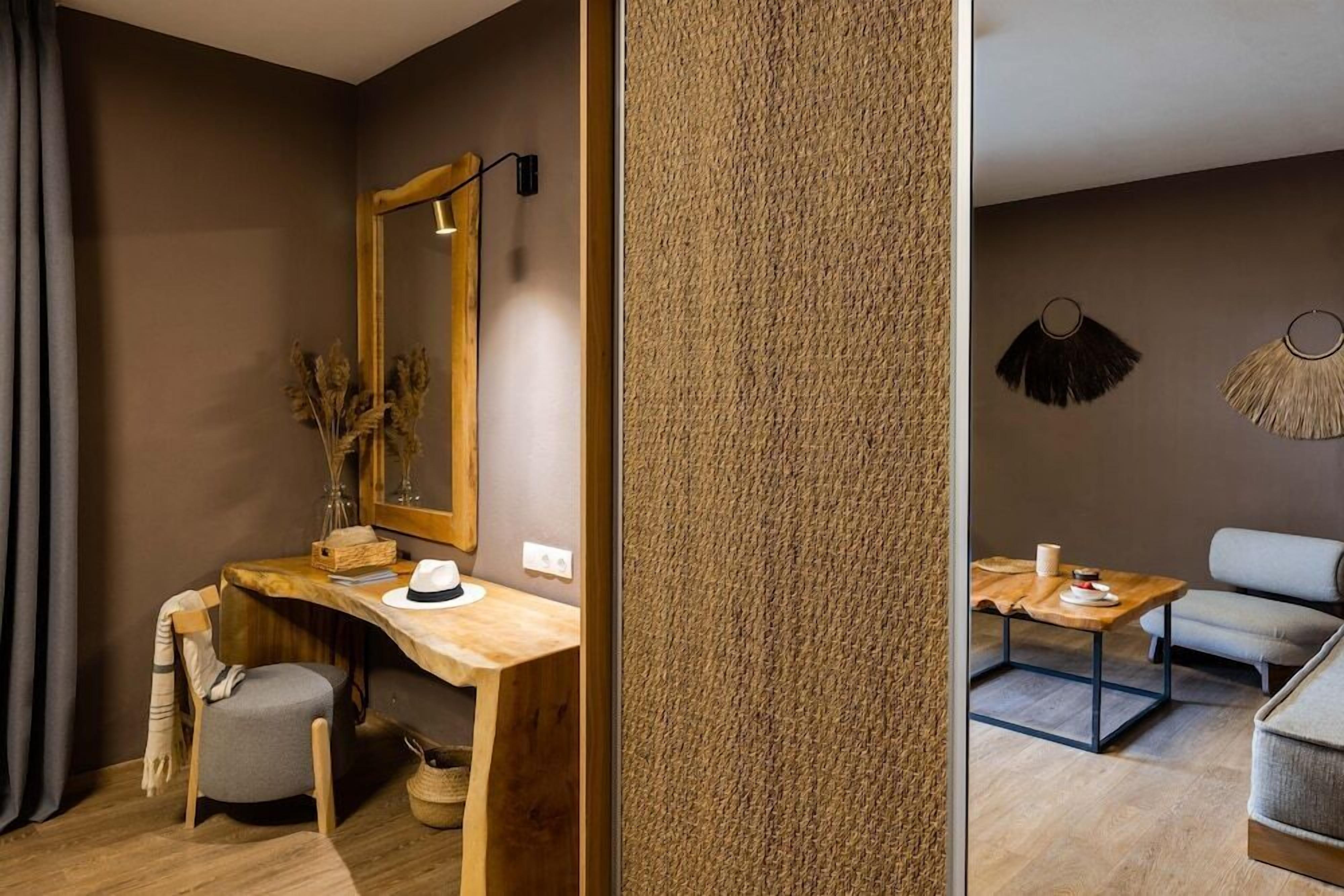 A room with a wooden desk, a chair, a mirror, a table with a cushion, and a sofa.