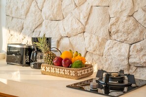 Uma bancada de cozinha com parede de pedra, uma cafeteira, uma cesta de frutas e um fogão a gás.