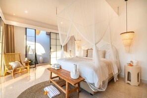 Ein modernes Schlafzimmer mit einem Himmelbett, einer Sitzecke mit Stuhl und Tisch sowie Blick durch eine Glastür.