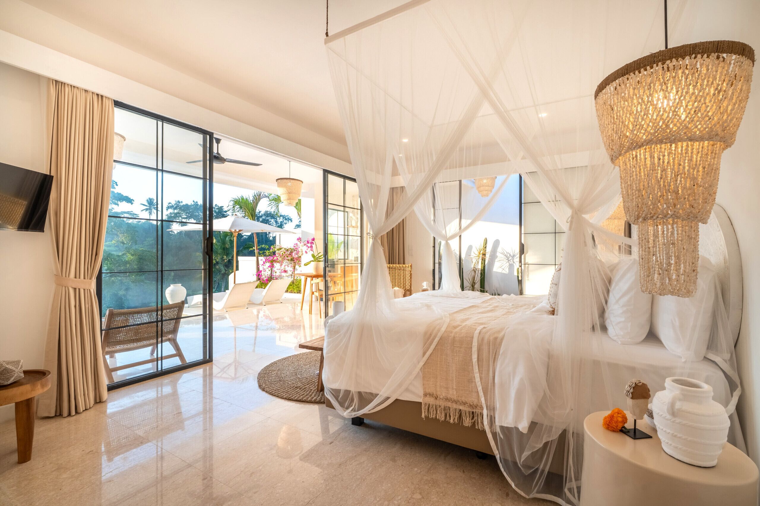 A bedroom with a large bed, a canopy, a view of the outdoors, and a chandelier.