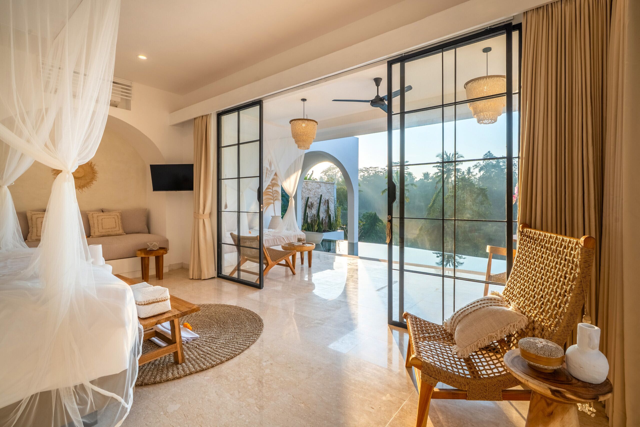 A spacious room with a large bed, a seating area with chairs, a television, and a view through large glass doors.