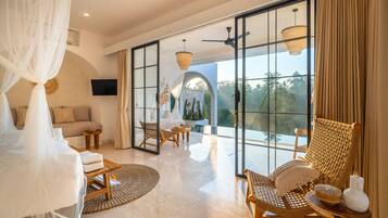A spacious room with a large bed, a seating area with chairs, a television, and a view through large glass doors.