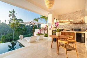 A modern kitchen with a stone backsplash, a dining area with a table and chairs, and a view of a lush garden and pool. - 2 Infinity Pools • Luxury Ubud 1br Villa • Jungle Paradise (Ubud)