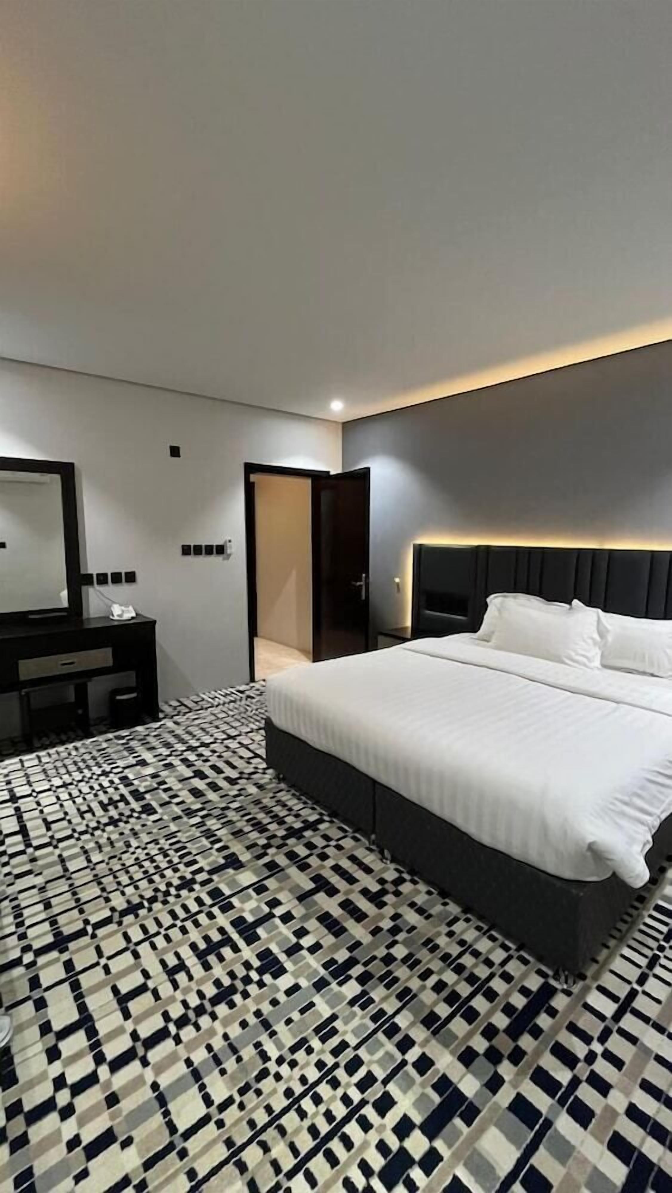 Une chambre d’hôtel moderne avec un grand lit, une table de chevet, un miroir et un sol à motifs.