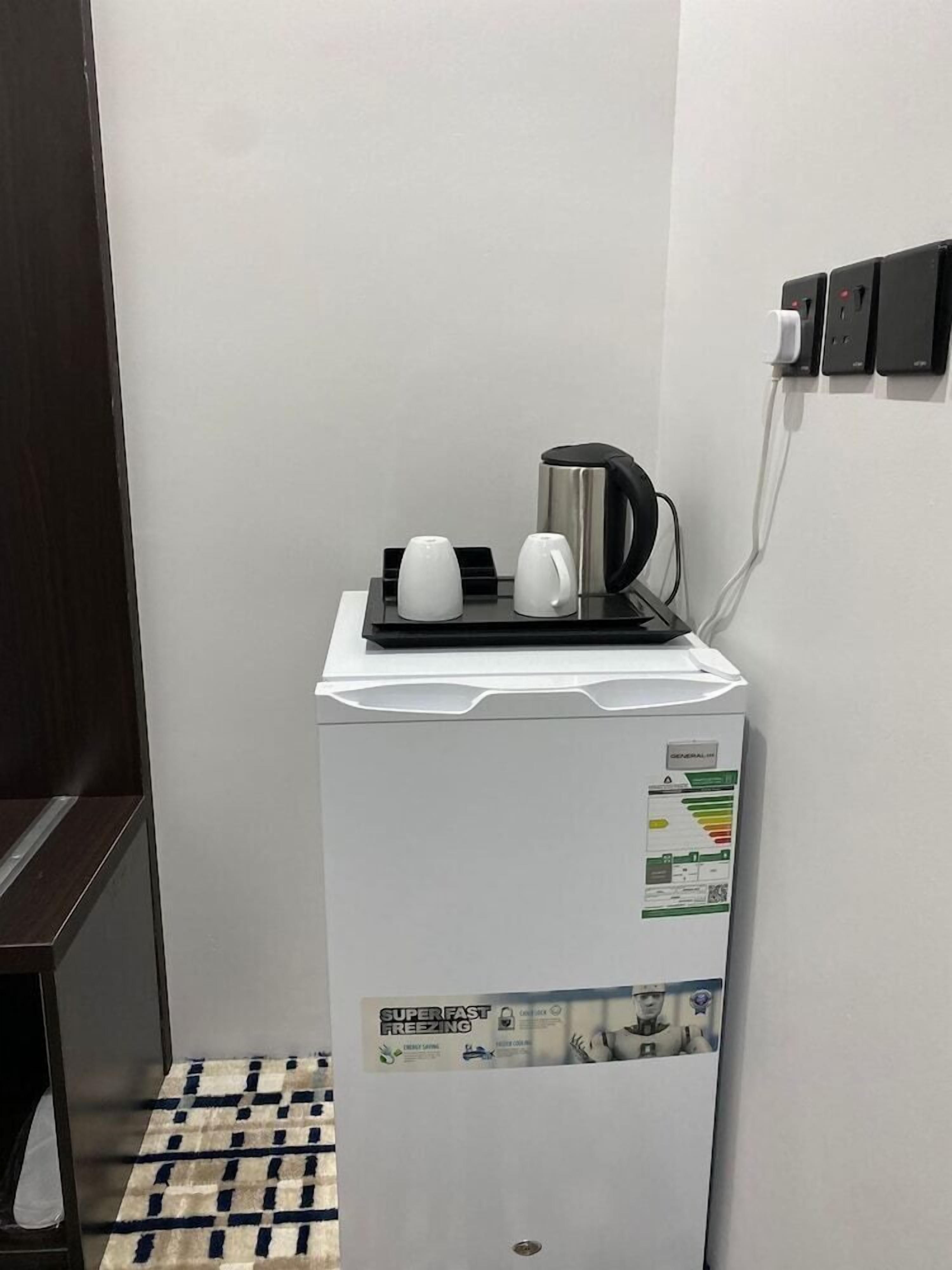 Uma geladeira compacta com cafeteira e chaleira em cima, uma mesa pequena e uma tomada na parede.