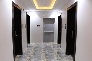 A hallway with a marble floor, two doors on each side, and a ceiling light fixture. - Qimam Park Hotel 4 (Abha)