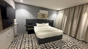 Una habitación de hotel moderna con una cama grande, un televisor de pantalla plana en la pared, una mesita de noche y un piso con diseño.