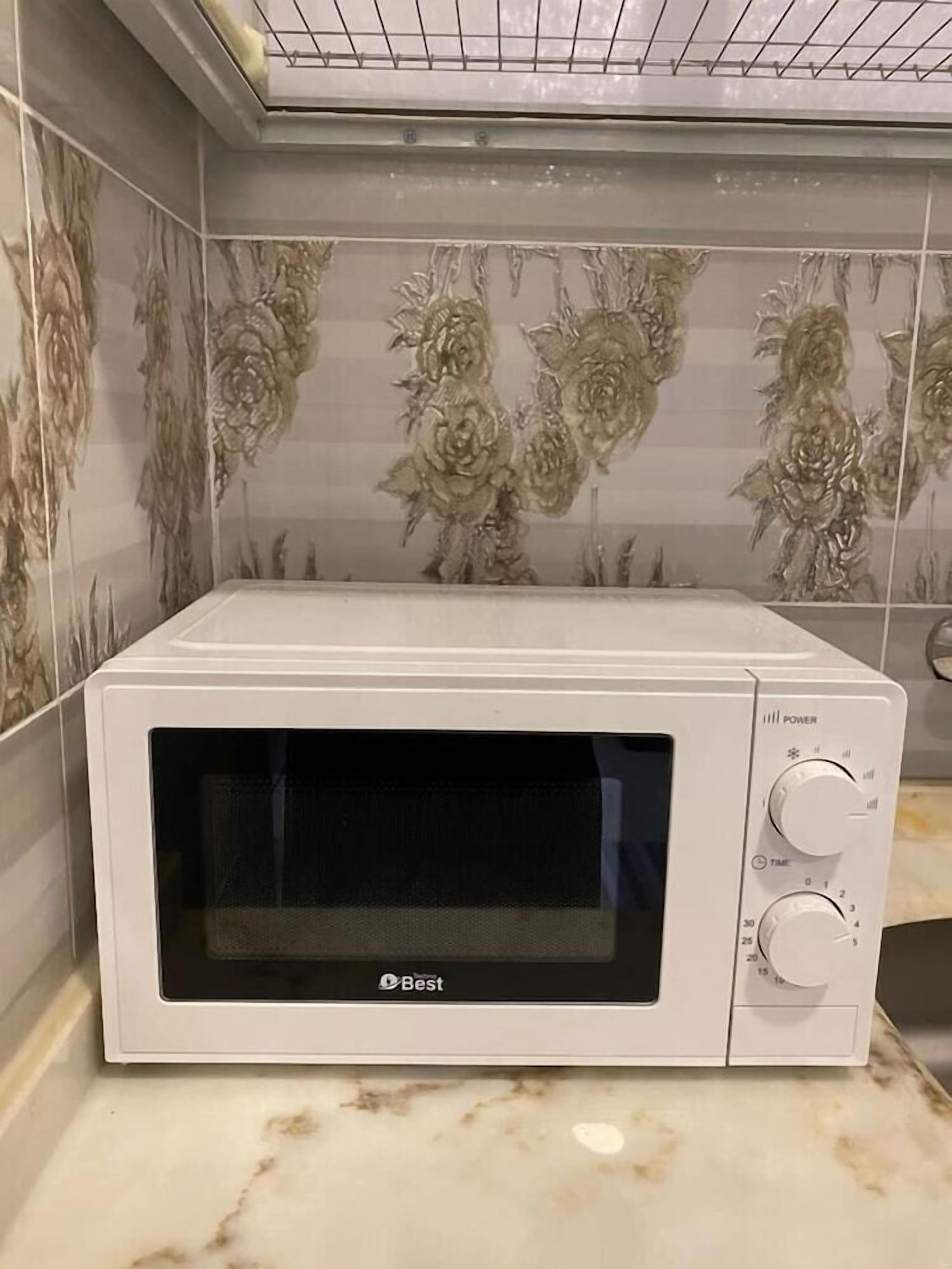Um forno de microondas Best branco sobre uma bancada de mármore com azulejos estampados com flores ao fundo.