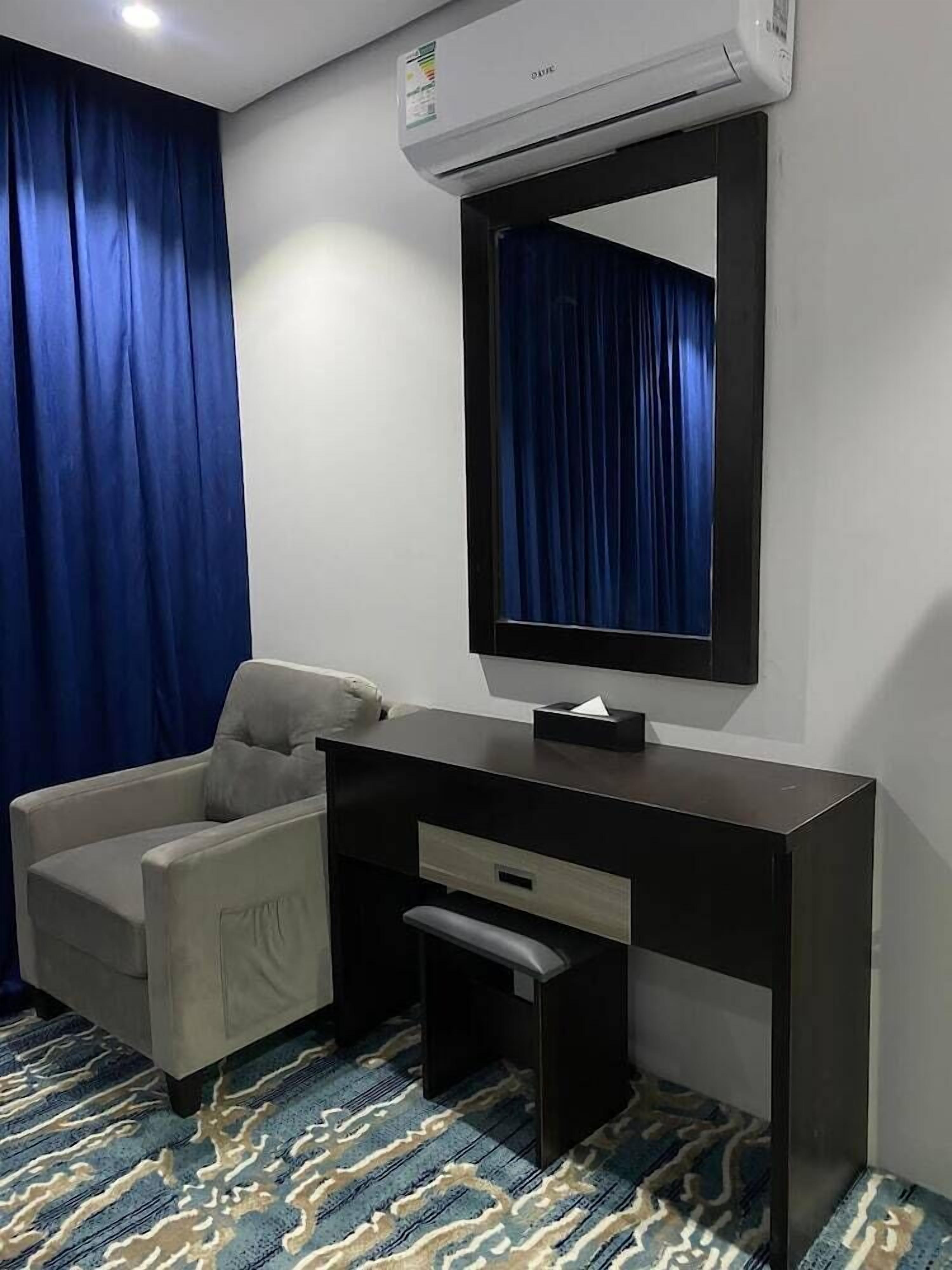 Habitación de hotel con escritorio, silla, aire acondicionado y alfombra estampada.