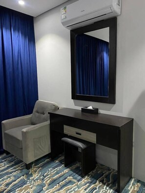 Ein Hotelzimmer mit Schreibtisch, Stuhl, Klimaanlage und einem gemusterten Teppich.