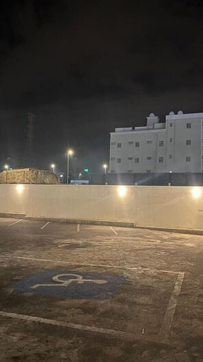 A parking area with a handicap parking symbol, a building in the background, and streetlights. - Qimam Park Hotel 4 (Abha)