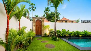 A well-maintained garden with a pool, a wooden door, and a stone wall.