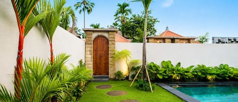A well-maintained garden with a pool, a wooden door, and a stone wall.