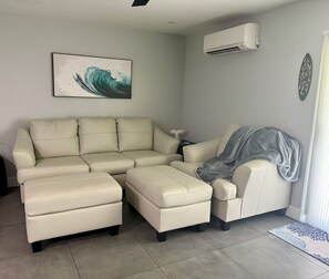 Een woonkamer met een hoekbank, een fauteuil en een grijze plaid.