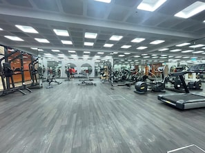 Uma academia com diversos equipamentos de exercício, espelhos e piso de madeira.