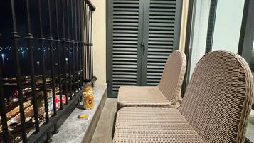 A balcony with wicker furniture, a closed door, and a view of a cityscape at night.