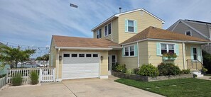 A two-story house with a garage, a front porch, and a small garden area. - Palm Trees & Great Sunsets! Exclusive Bayfront w/ Huge Outdoor Living Area&Docks (Stone Harbor)