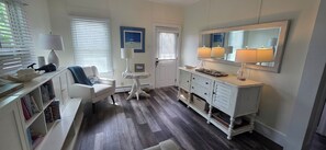 A well-lit room with a white sofa, a small round table, a white dresser with drawers, and a large mirror above the dresser. - Palm Trees & Great Sunsets! Exclusive Bayfront w/ Huge Outdoor Living Area&Docks (Stone Harbor)
