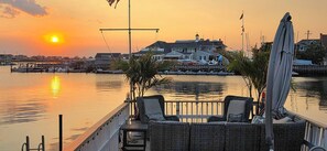 A waterfront patio with wicker furniture, a view of the sunset, and a marina in the background. - Palm Trees & Great Sunsets! Exclusive Bayfront w/ Huge Outdoor Living Area&Docks (Stone Harbor)