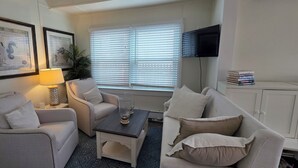 A living room with two armchairs, a coffee table, a lamp, a TV, and framed artwork on the wall. - Palm Trees & Great Sunsets! Exclusive Bayfront w/ Huge Outdoor Living Area&Docks (Stone Harbor)