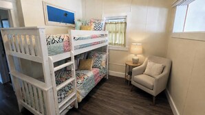 A room with bunk beds, a small table with a lamp, and a chair. - Palm Trees & Great Sunsets! Exclusive Bayfront w/ Huge Outdoor Living Area&Docks (Stone Harbor)