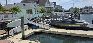 Un port esportiu amb vaixells amarrats, una passera de fusta i cases al fons.