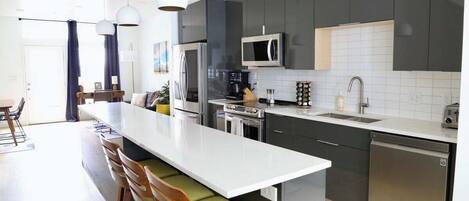 Una cocina moderna con una isla central, electrodomésticos de acero inoxidable y taburetes de bar.