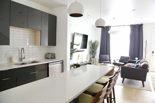 Une cuisine moderne dotée d’un îlot central, de meubles de rangement aux couleurs sombres et d’un coin repas avec un canapé et des chaises.