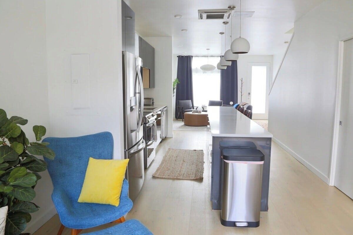 A modern kitchen with stainless steel appliances, a dining area with a table and chairs, and a blue chair with a yellow pillow.