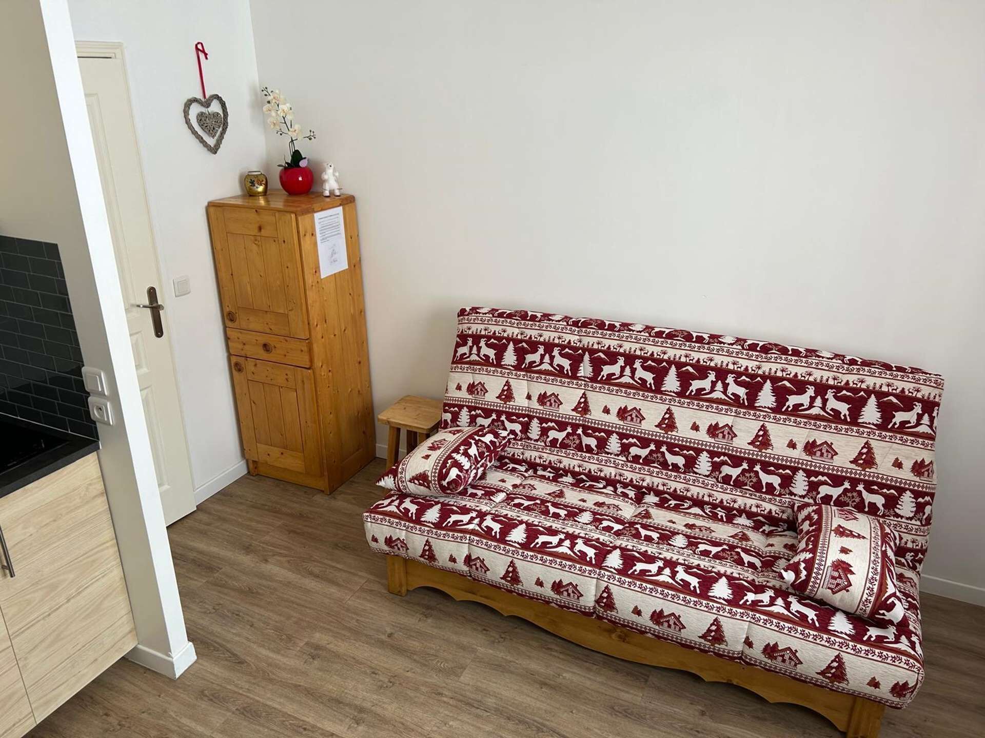 Um quarto com um armário de madeira, um sofá com padrão vermelho e branco e um banquinho de madeira.