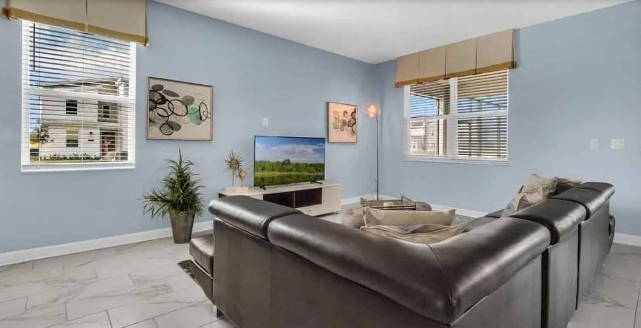 A living room with a dark leather sofa, a flat-screen TV, and artwork on the walls.