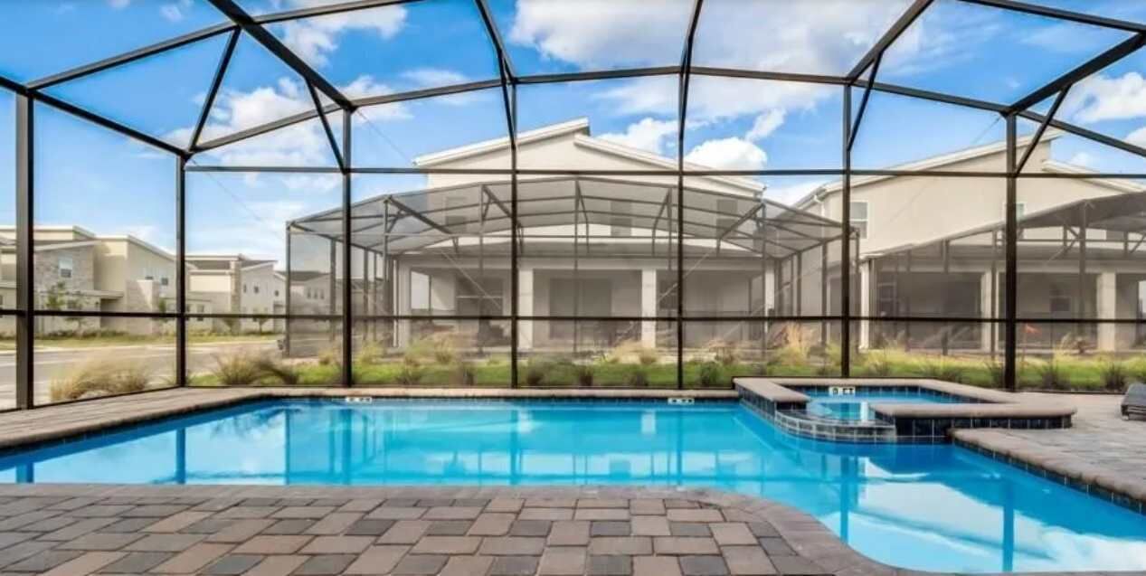 Una piscina con cerramiento de vidrio, rodeada por una zona pavimentada y un cielo despejado.