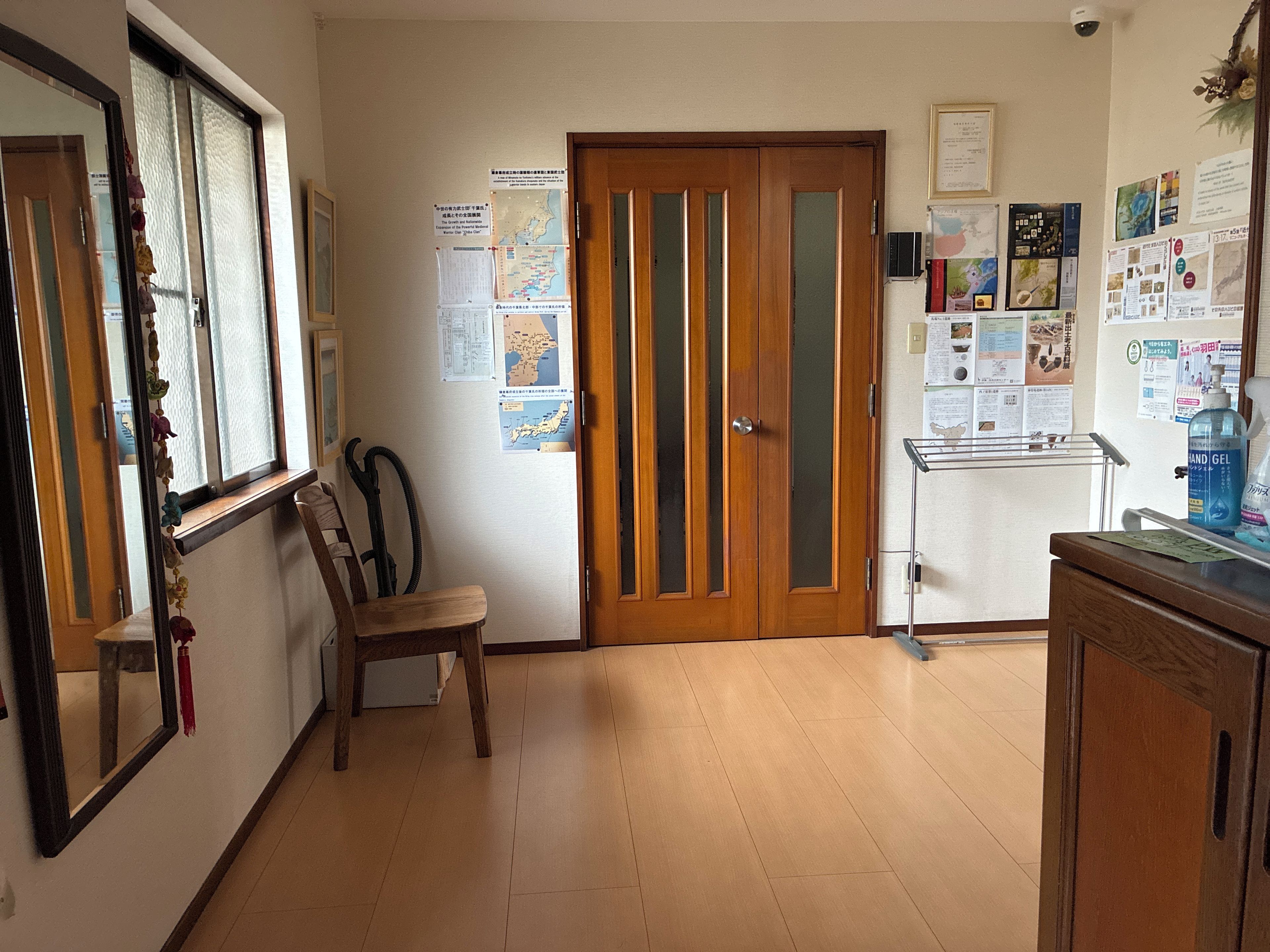A hallway with a wooden door, a chair, and a small table with a bottle of hand gel.