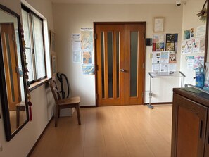 A hallway with a wooden door, a chair, and a small table with a bottle of hand gel. - MORE&MORE (Sakura)