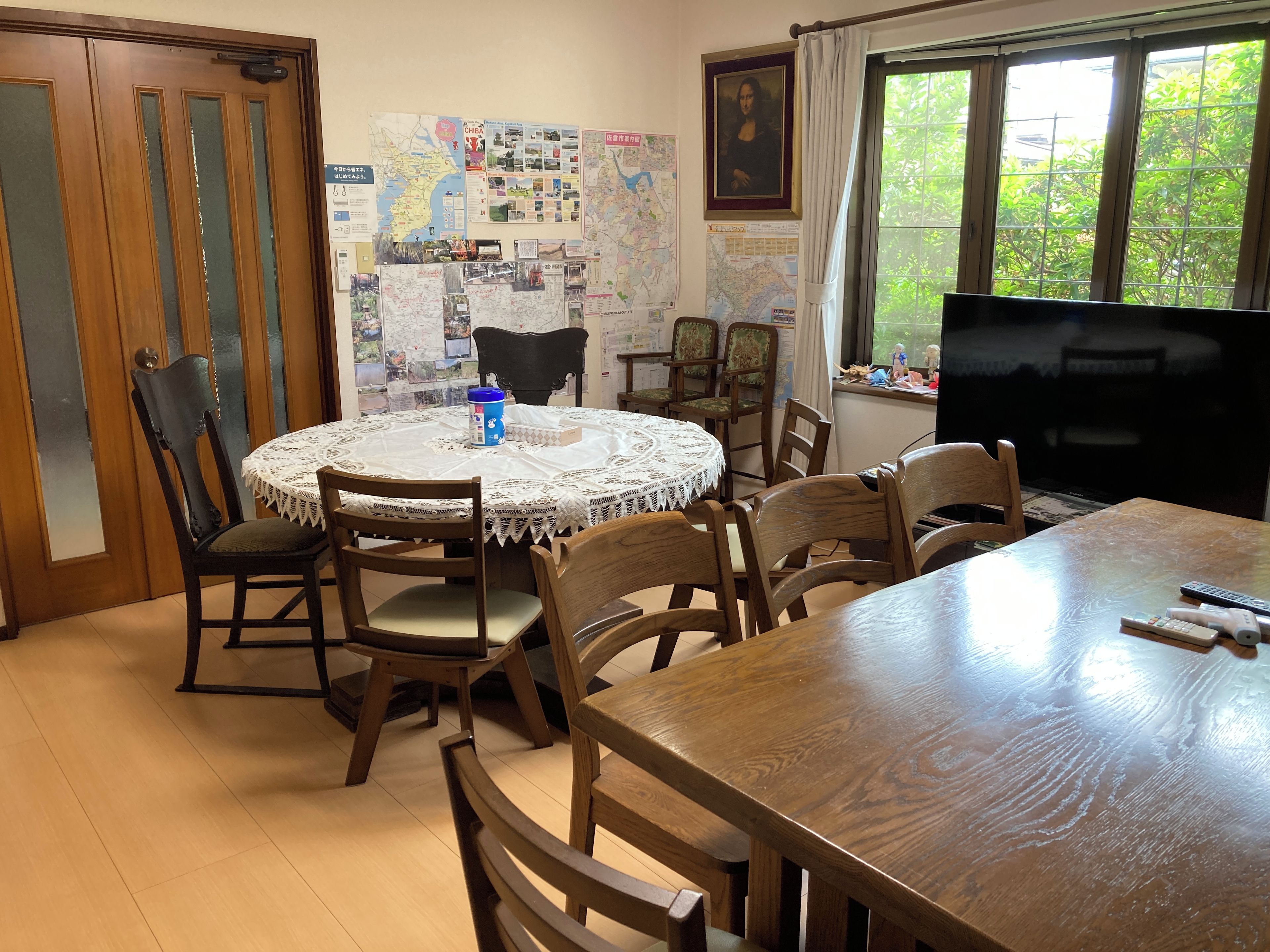 A dining area with a round table, chairs, a television, and a wall with maps and pictures.