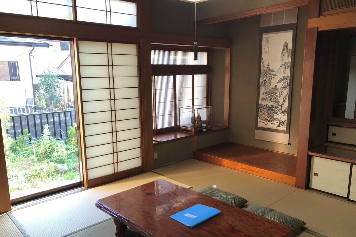 Ein traditioneller japanischer Raum mit Tatami-Böden, einem Holztisch mit einer blauen Ordner und verschiebbaren Shoji-Türen, mit Blick ins Freie.