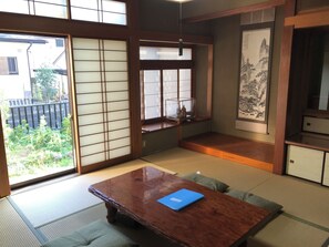 Ein traditioneller japanischer Raum mit Tatami-Böden, einem Holztisch mit einer blauen Ordner und verschiebbaren Shoji-Türen, mit Blick ins Freie.