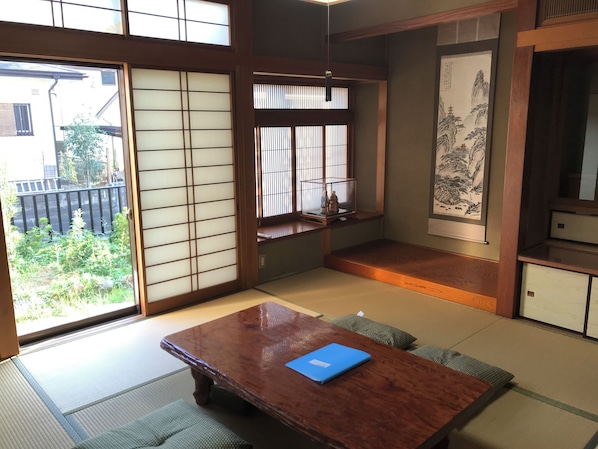 Una habitación japonesa tradicional con suelo de tatami, una mesa de madera con una carpeta azul, puertas correderas shoji y vistas al exterior.